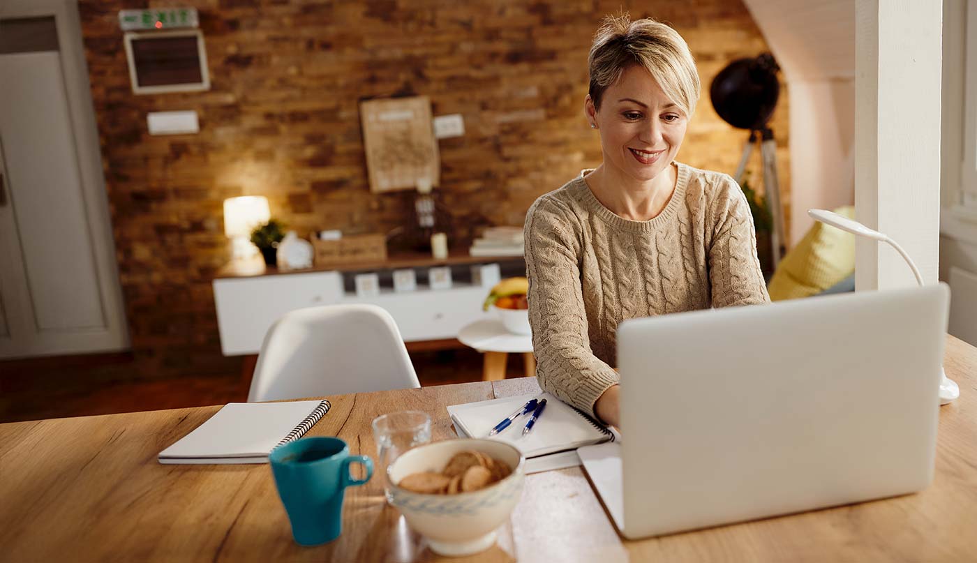 Doctor using a laptop at a wooden table in a home setting.