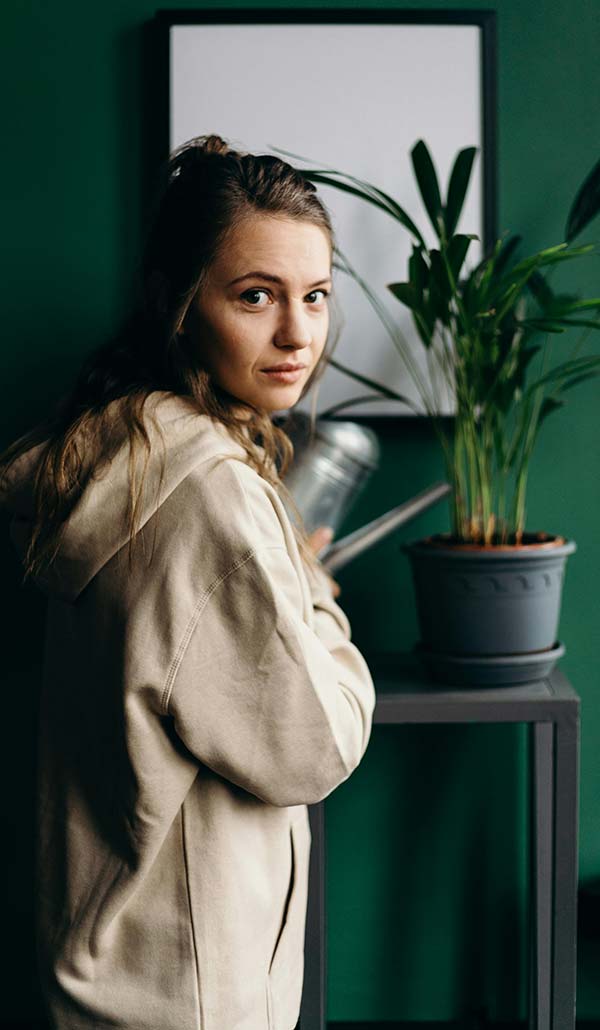 Woman in a room with green walls and a plant on a table waiting for her cannabis doctor to call.