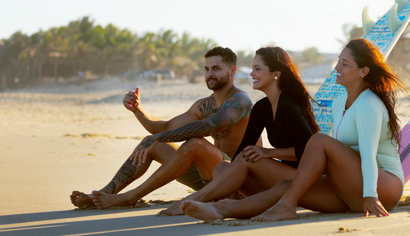 Three people sitting on a beach with surfboards, enjoying a sunny day.